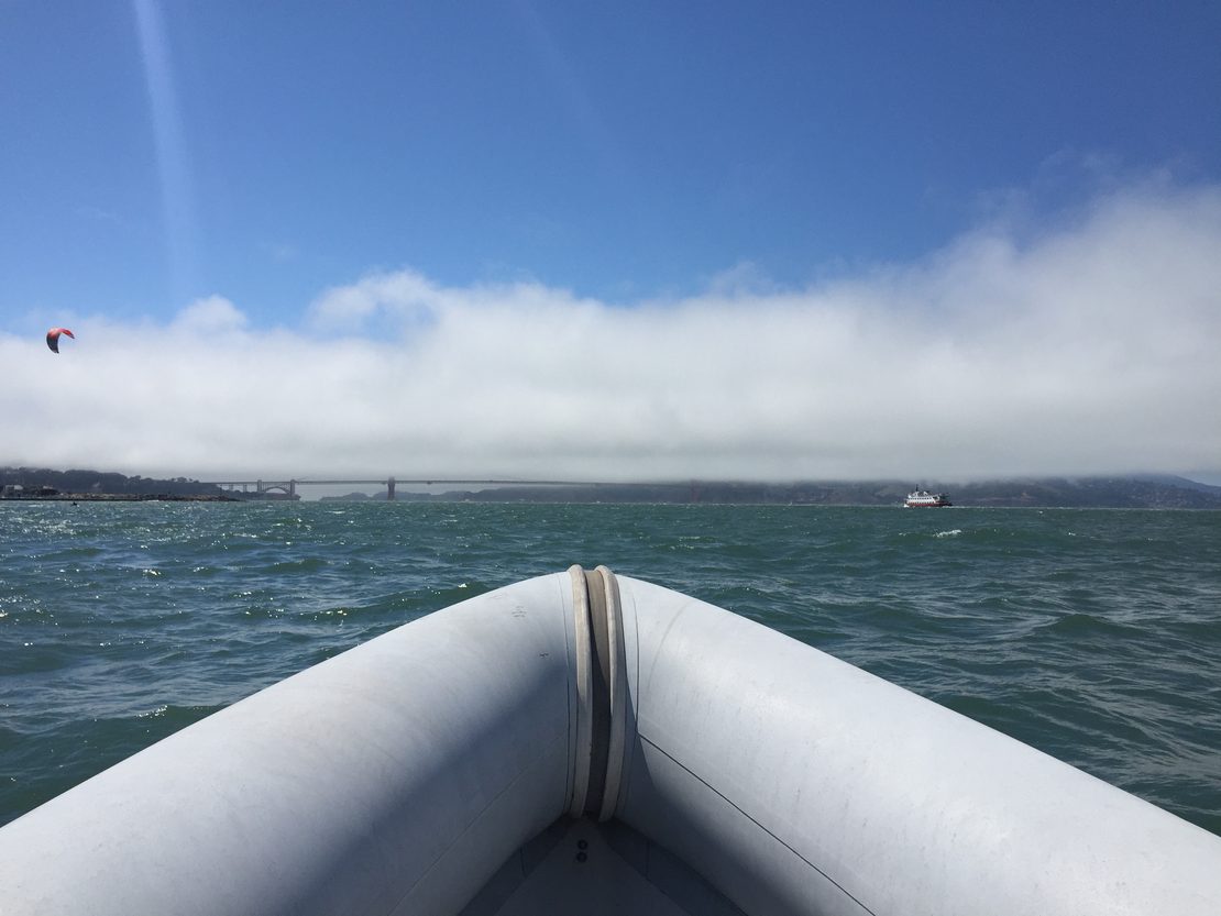 A small, Rigid Hull Inflatable Boat skims across the bay looking towards The Golden Gate Bridge.
